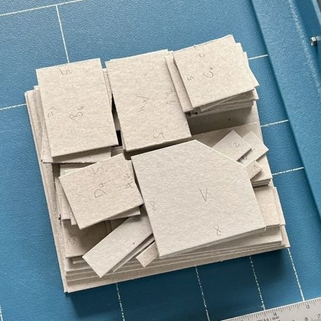 Workshops Anleitungen Material-Sets Stapel von rechteckigen, grauen Papierblättern auf blauer Unterlage.