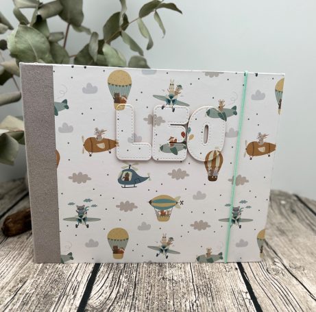 Individualisierbare Projekte Ein fröhliches Notizbuch mit Luftballons und Flugzeugen auf einem gemusterten Cover.