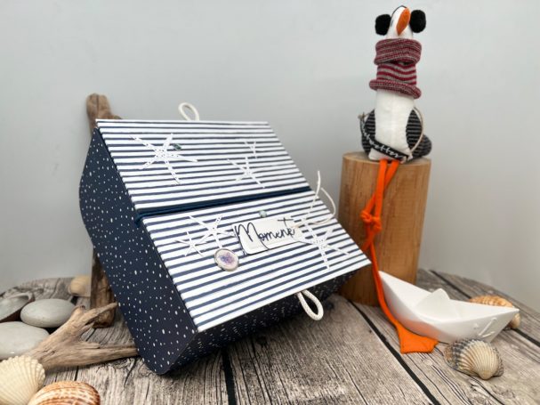 Fertige Werkstücke Blau-weiß gestreifte Box mit maritimen Motiven neben einer dekorativen Möwe.